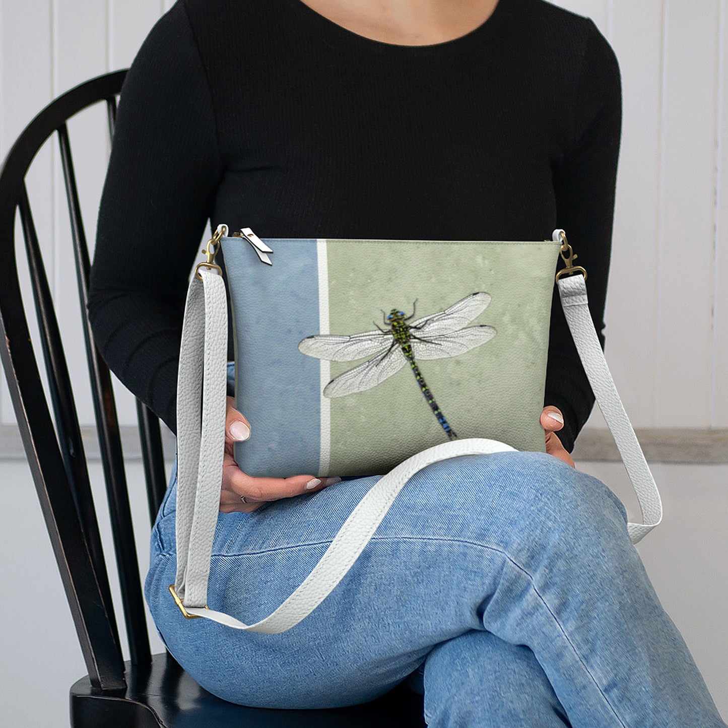 Person holding a crossbody bag with a dragonfly design