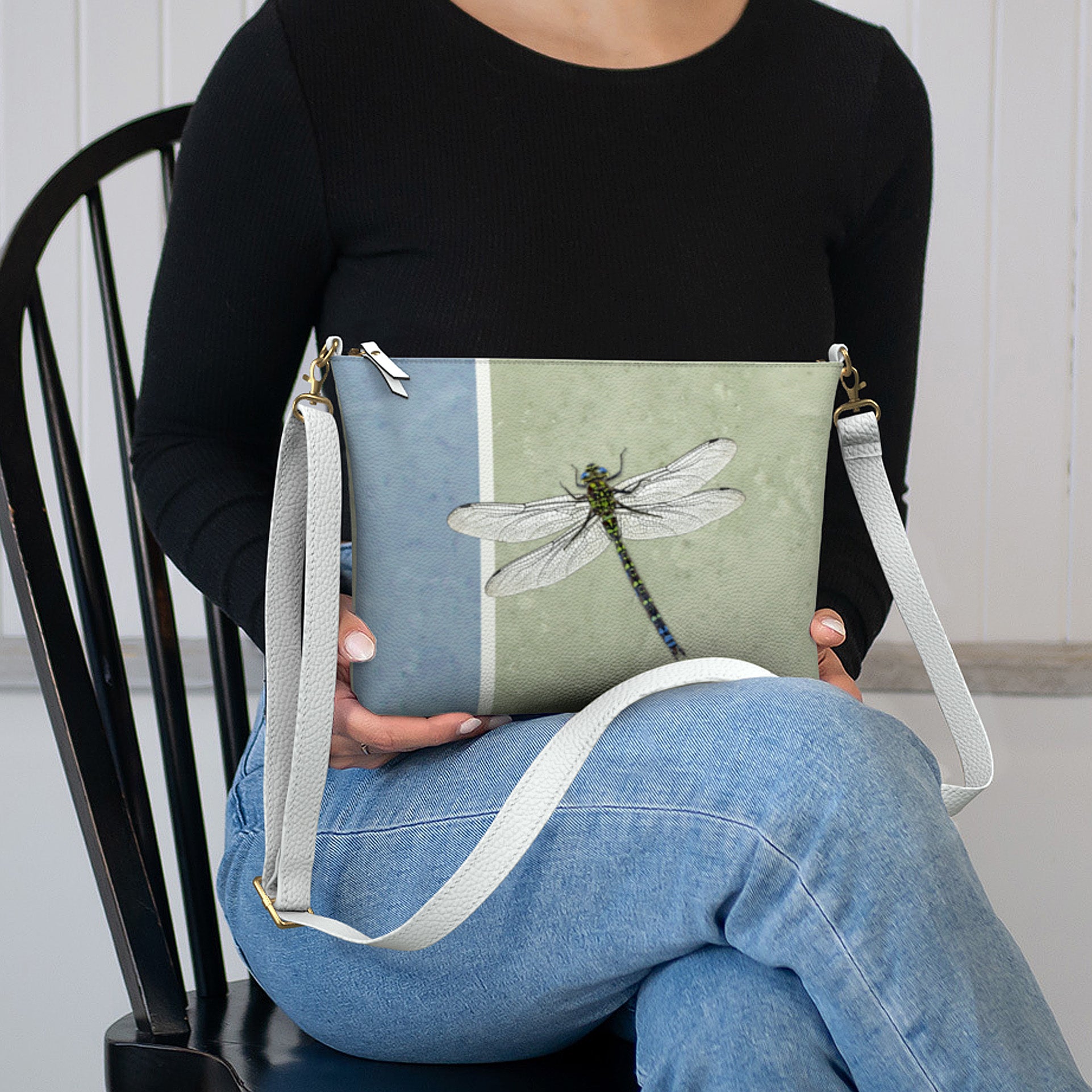 Person holding a crossbody bag with a dragonfly design
